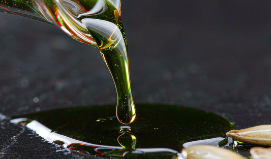 Extreme macro of dark green pumpkin seed oil being poured, glowing red at the thin edges on slate