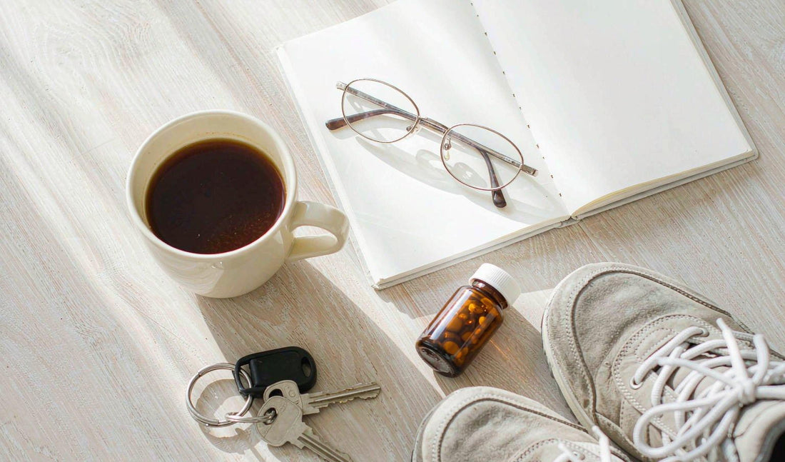 Overhead flat lay of a planner, glasses, coffee, keys and walking shoes on a pale oak desk in sunlight