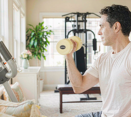A man in his 50s lifting a light dumbbell in a bright airy home gym, side view, no face