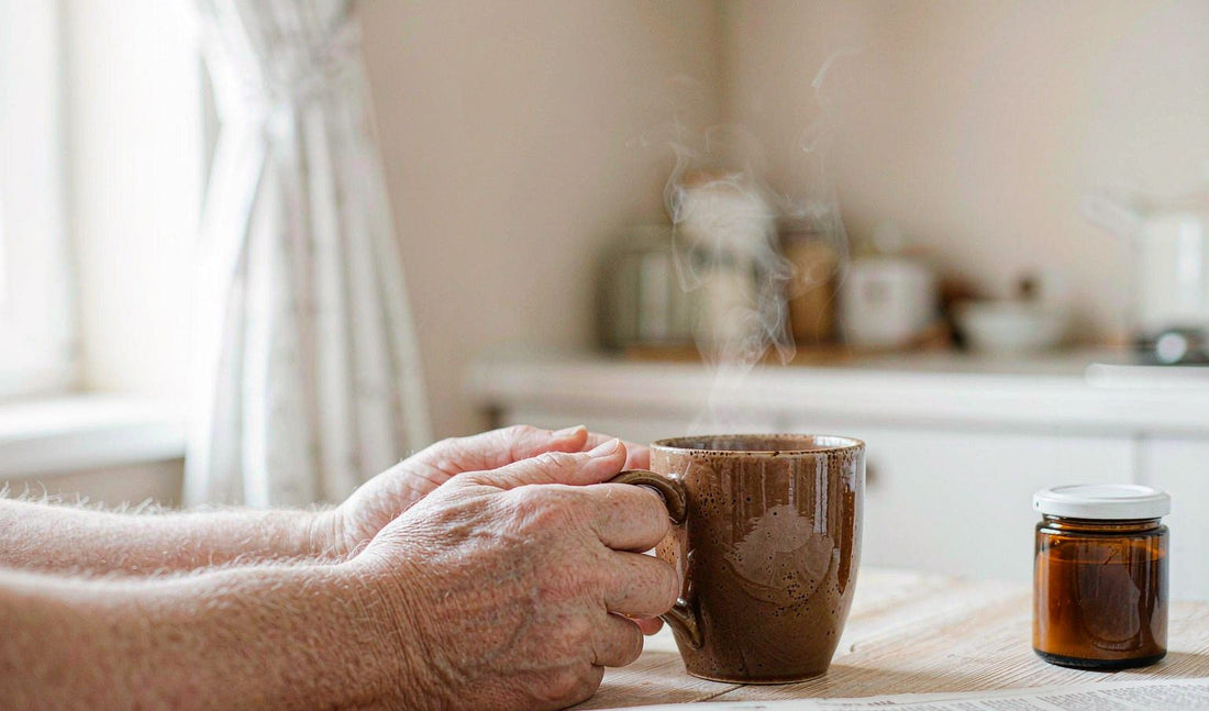 A retired man's fair-skinned hands holding a warm mug at a bright kitchen table in the morning