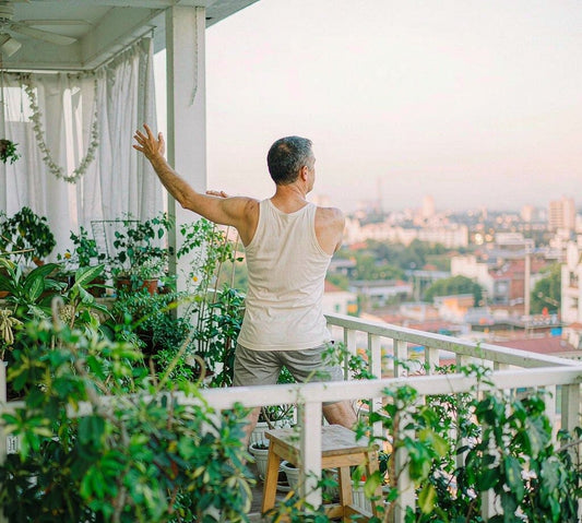 A man in his 50s stretching on a bright airy balcony at sunrise, seen from behind