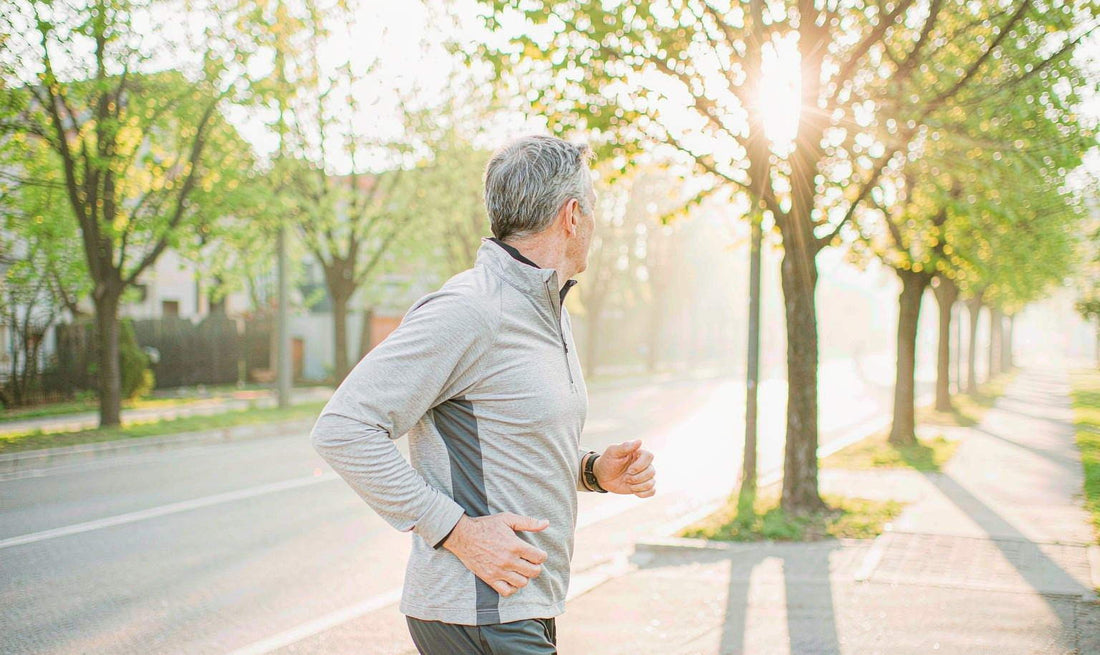 A fit man in his late fifties walking a tree-lined suburban street at dawn, seen from the side, face turned away