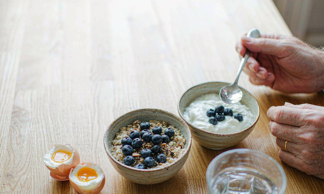 A man's hands reaching for a spoon at a bright kitchen breakfast table, no face in frame