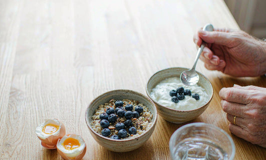 A man's hands reaching for a spoon at a bright kitchen breakfast table, no face in frame
