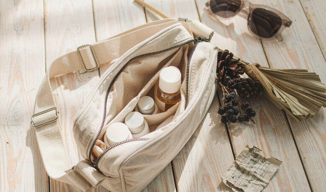 An open canvas travel pouch with an amber dropper bottle, dried berries and a palm leaf on a bench