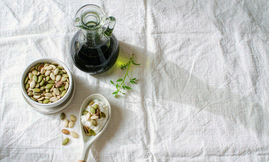 Flat lay of pumpkin seeds, cold-pressed pumpkin seed oil and yoghurt on white linen